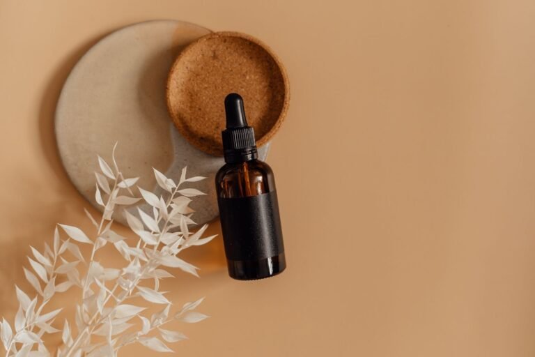 Unlabelled amber dropper bottle on cork and stone coasters with dried white leaves on a warm beige background
